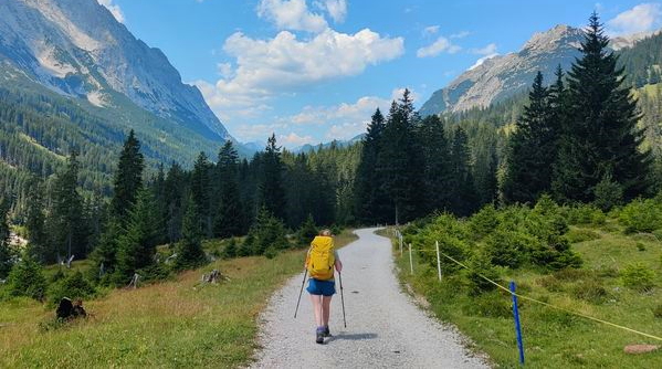 A hiker with yellow backpack on a paved path walking into Ehrwald on the self-guided Adlerweg trip with Alpine Exploratory