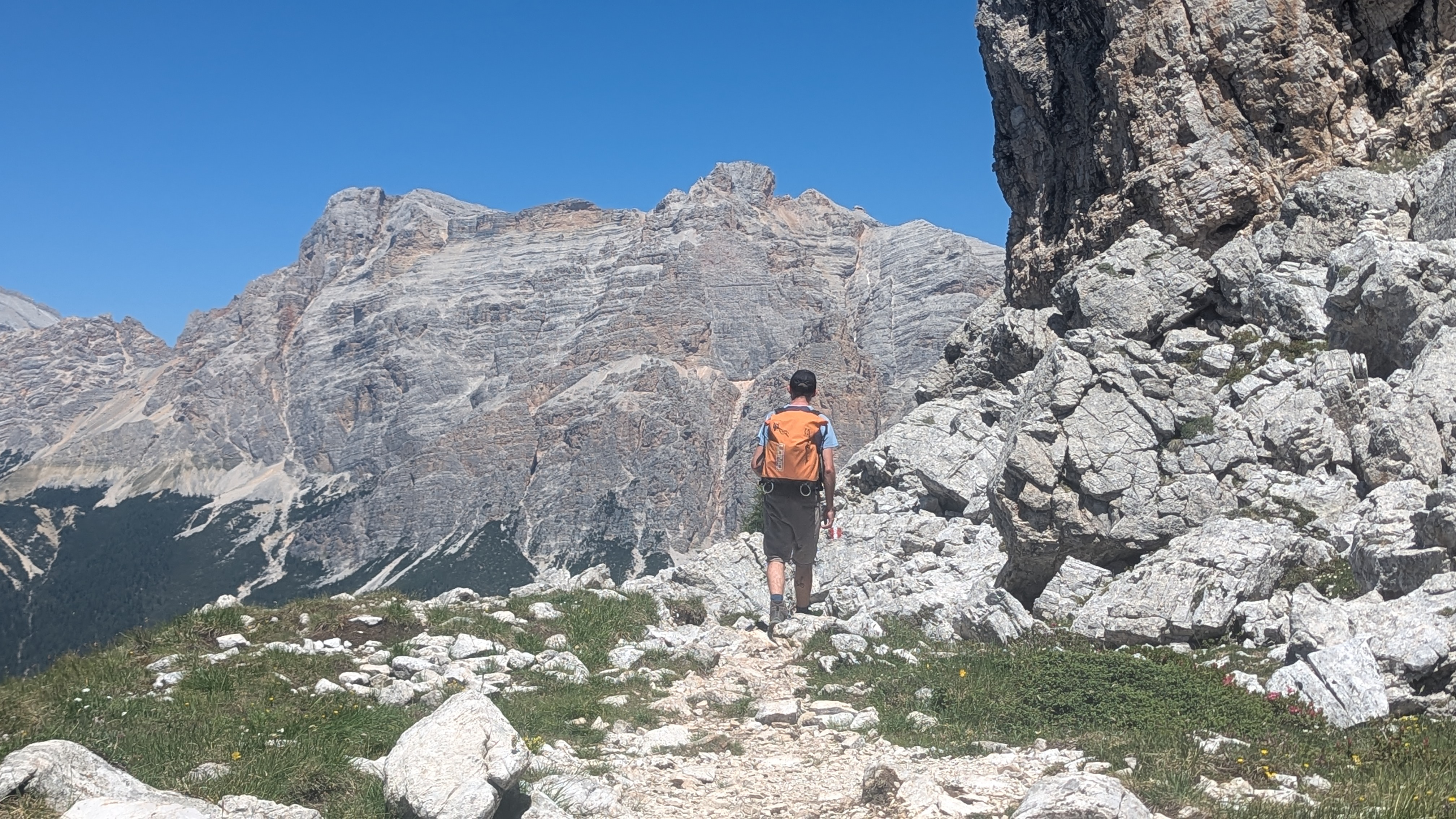 A hiker descends around rocky outcrops on the edge of the Pralongia Platau