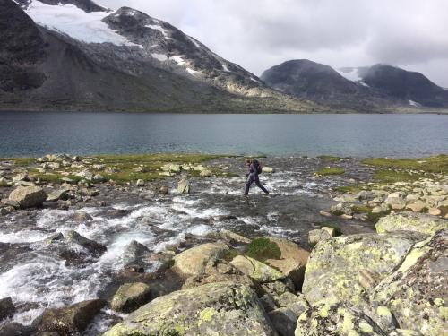 trekker crosses a wide river flowing into a lake