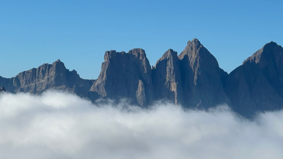 A bold, dark, rocky ridge with clouds below and sky above, from the AV2
